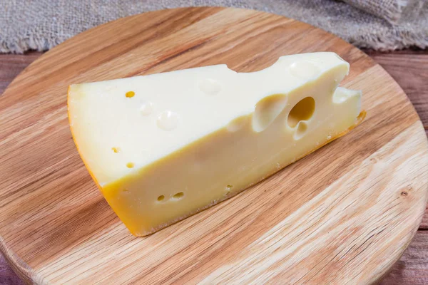 Piece of Swiss-type cheese on the wooden cutting board — Stock Photo, Image