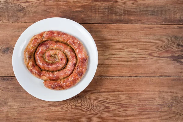 Запечённая свиная колбаса на блюде слева на деревенском столе — стоковое фото