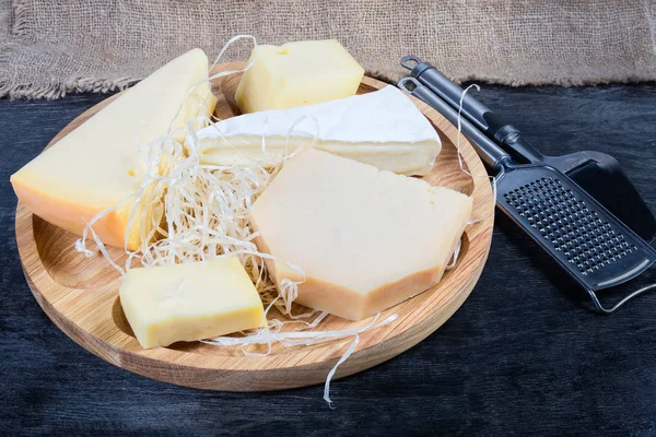 Different varieties of cheese on wooden dish, slicer and grater