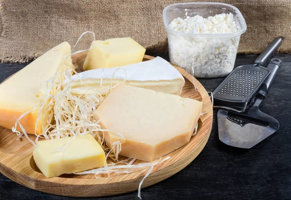 Différents fromages sur plat en bois, fromage cottage, trancheuse et râpe — Photo