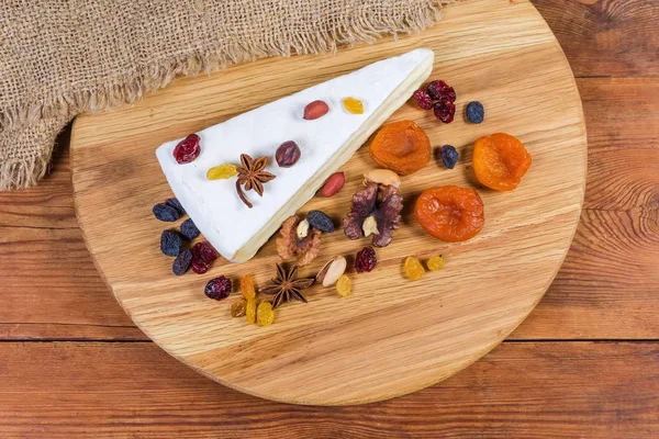 Queijo Brie entre nozes e frutas secas na tábua de corte — Fotografia de Stock