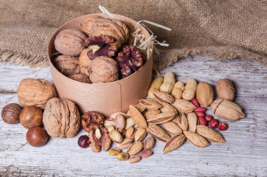 Yuvarlak ahşap kutuda ve onun yanında çeşitli fındıklar.