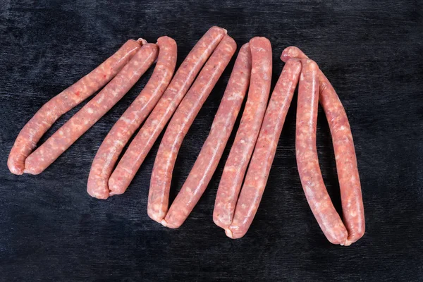 Uncooked thin long pork sausages on the black surface — Stock Photo, Image