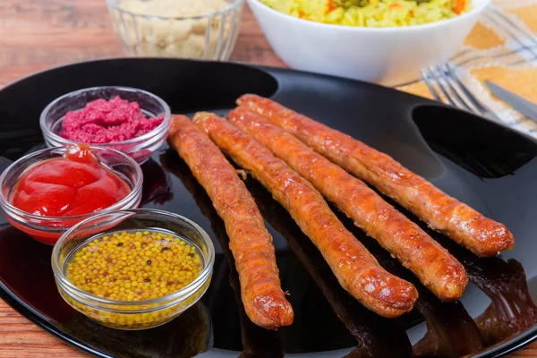 Grilled pork sausages, condiments on dish closeup in selective focus — Stock Photo, Image