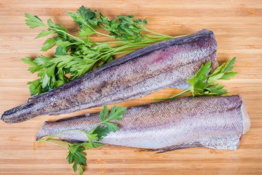 Ahşap yüzeyde maydanozların arasında pişmemiş hake leşleri.