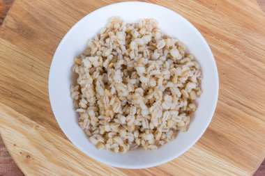 Pearl barley porridge in bowl on wooden surface, top view clipart