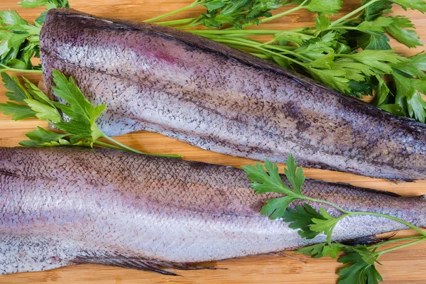 Pescada não cozida com salsa na tábua de corte, fragmento, vista superior — Fotografia de Stock