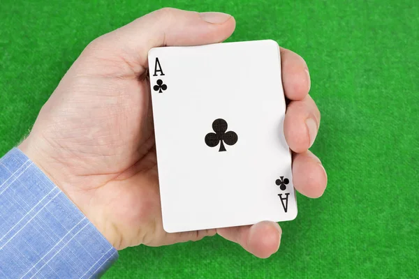 Deck of playing cards in a male hand with ace of clubs face-up on a blurred background of green game table