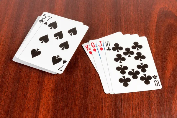 Combination of playing cards - king, queen and jack of diamonds and ten of clubs against the cards deck on the wooden table