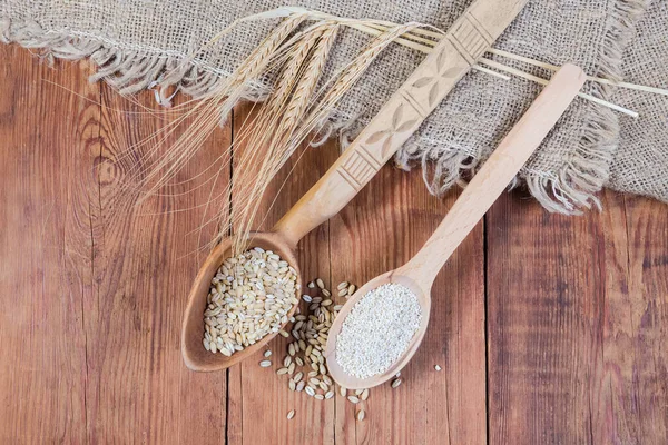 2本の木製のスプーンで生の粉砕大麦の穀物と真珠の大麦 素朴なテーブルの上にバラップに大麦の耳 トップビュー — ストック写真