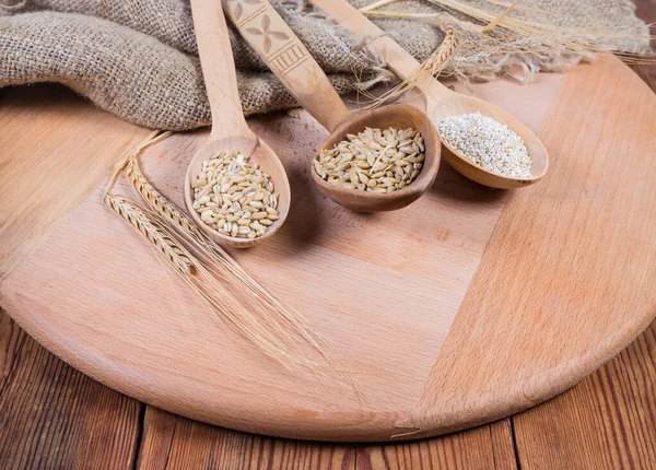 Raw crushed barley groats, pearl barley and whole barley grains in different wooden spoons on the wooden serving board on rustic table