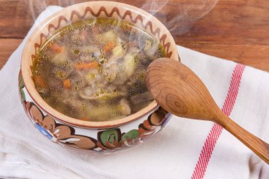 Kil kaplı kasede mantarlı taze hazırlanmış karabuğday çorbası, kırsal masada tekstil peçetesinde tahta kaşık.