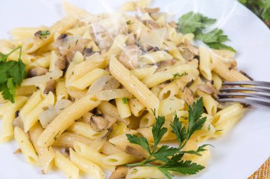 Kaynamış silindir şekilli makarna, kızarmış mantar ve soğanla karıştırılmış beyaz tabakta, seçici odak noktasında parça yakın plan.