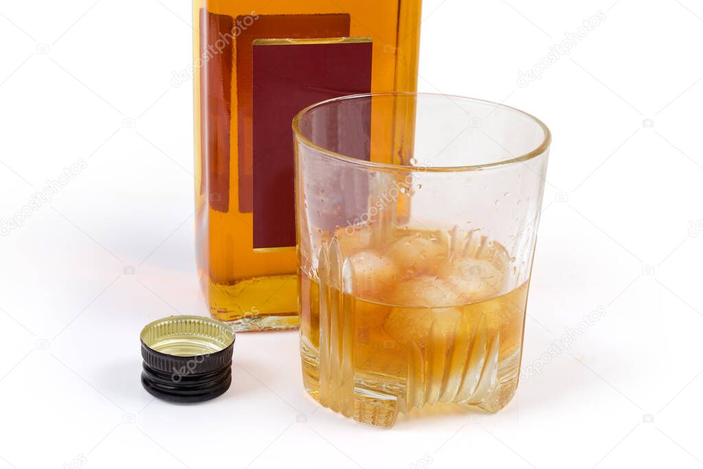 Glass of whisky with pieces of ice against the fragment of whisky bottle and  black screw cap on a white background