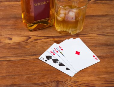 Elmas ve maça takımlarının birleşimi eski kırsal masada yüzükoyun uzanmış buz ve şişeyle cam viskiye karşı.