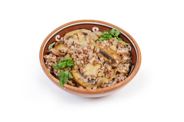Freshly boiled buckwheat porridge mixed with fried chopped mushrooms and onions in the clay glazed dish on a white background
