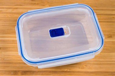 Boş cam dikdörtgen havalandırmalı yiyecek depolama kabı. Ahşap bir yüzey üzerinde şeffaf plastik kapaklı, üst görünüm.