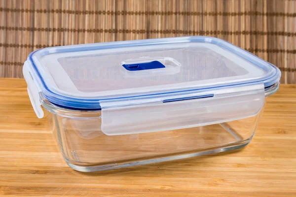 Empty glass rectangular ventilated food storage container with translucent plastic lid on a wooden surface