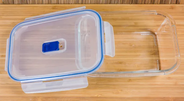Empty glass rectangular ventilated food storage container with partly opened translucent plastic lid on a wooden surface, top view