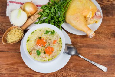 Beyaz kasede ince vermicelli ev yapımı tavuk çorbası, kaşık ve kırsal masada biraz ham malzeme, üst manzara.