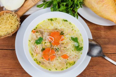 Beyaz kasede ince vermicelli ev yapımı tavuk çorbası, kırsal masadaki hammaddelerin arasında kaşık, üst manzara, arka plan.