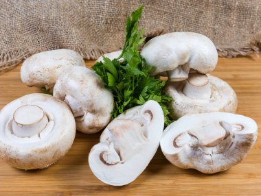 Çuval bezine karşı ahşap yüzey üzerinde birkaç tam ve yarım büyük çiğ taze ekilmiş beyaz düğmeli mantar.