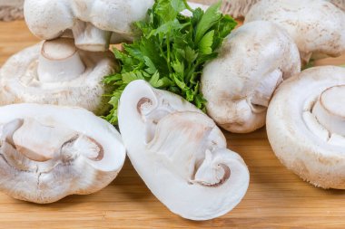 Ahşap yüzeye yakın plan, parça, arkaplan üzerinde büyük, çiğ, taze mantar ve maydanoz yığını.