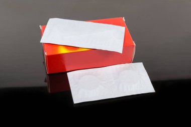 Kağıt paketler dolusu ilaç hapları ve koyu renk yansıtıcı yüzeyde kırmızı karton kutular.