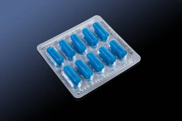 Blister pack with a pharmaceutical product in the form of blue pills close-up on the dark reflecting surface