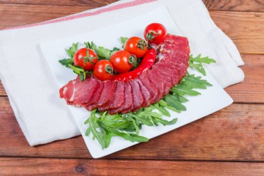 Kurutulmuş domuz budu dilimleri taze otların arasında ve kırsal masadaki beyaz peçetenin üzerinde kiraz şeklinde domatesler.