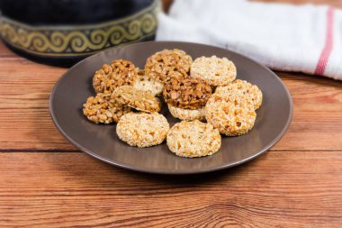 Kırsal masadaki kahverengi kabın içinde karamelleştirilmiş şeker, ayçiçeği ve susam tohumlarından yapılmış yuvarlak gevrek şekler, seçici odak noktasında yakın plan peçeteyle.