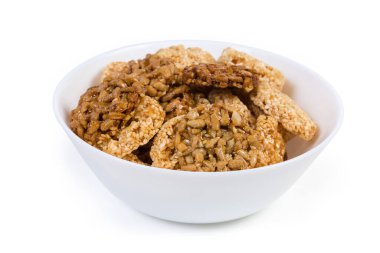 Beyaz arka planda beyaz kasede karamelize şeker, ayçiçeği ve susam tohumlarından yapılmış yuvarlak gevrek şekerler, seçici odak noktasında yakın plan.