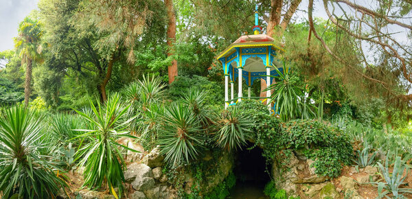 Gazebo over the grotto among the lawn with succulents against the coniferous trees in the Nikitsky Botanical garden, panoramic view