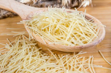 Pişmemiş, ahşap kaşıkta Filini makarna olarak bilinen çok ince kesitli yuvarlak makarna ve yanında dağınık, seçici odak noktasında yakın çekim