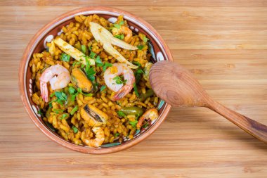 Ahşap yüzeyinde ahşap kaşıkla kil kasede pişirilmiş deniz ürünleri paella.