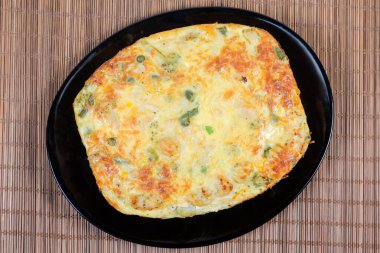 Fırınlanmış sebze güveci fırın kabından alınıp bambu masa paspasındaki siyah tabakta servis edilir.