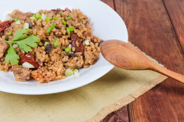 Beyaz tepside etli ve mantarlı paella pilavı, kırsal masada ahşap kaşık, yakın plan tabak.