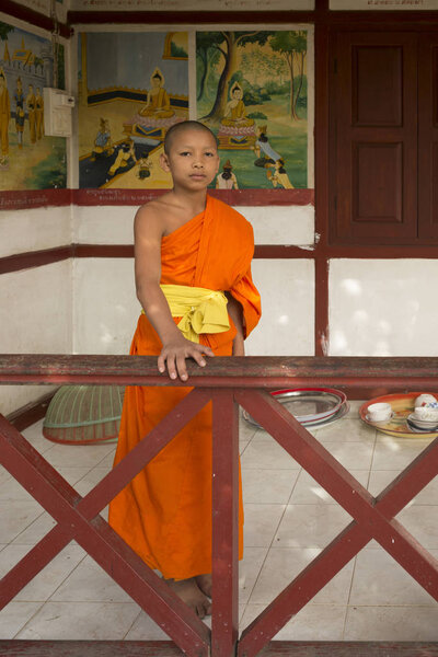 Portrait of boy monk standing by railing at temple, Luang Prabang, Laos