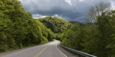 Empty road amidst trees by hills, Pleasant Bay, Cape Breton Highlands National Park, Cape Breton Island, Nova Scotia, Canada clipart