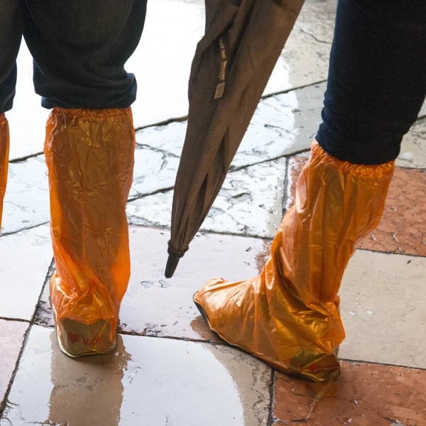 Low section of people wearing plastic rain shoes on sidewalk, Venice, Veneto, Italy