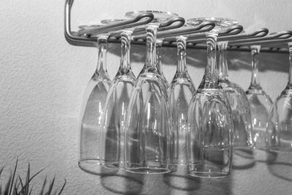 Czarno-białe zdjęcie grupy przezroczystych kieliszków do wina z pięknymi refleksami zawieszonymi na szarej metalowej półce — Zdjęcie stockowe