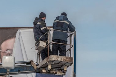 Yekaterinburg, Sverdlovsk / Rusya - 11 01 01 2019: Mavi ceketli iki işçi gökyüzü arkaplanına ilan panosu astı