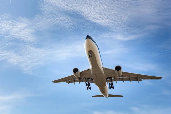 Белый и серебристый самолет с шасси приземляется на голубом небе на фоне облаков — стоковое фото