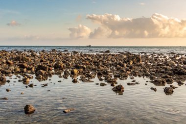 Güzel bir turkuaz deniz, ıslak turuncu taşlar ve sarı gün batımlı tekneler.