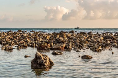 Güzel bir turkuaz deniz, ıslak turuncu taşlar ve sarı gün batımlı tekneler.