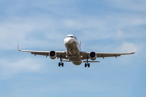 Şaseli beyaz ve gümüş renkli uçak bulutlu arka planda mavi gökyüzüne iniyor.