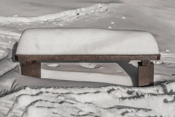 Drewniany pomalowany brązowy kolor piękna ławka stoi z białym śniegiem w parku w zimie — Zdjęcie stockowe