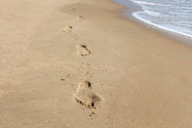 İzleri ve ayak izleri olan güzel sarı kumlu sahil, güneş ışığı ve dalgalarla turkuaz deniz kenarındadır.