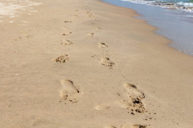 İzleri ve ayak izleri olan güzel sarı kumlu sahil, güneş ışığı ve dalgalarla turkuaz deniz kenarındadır.