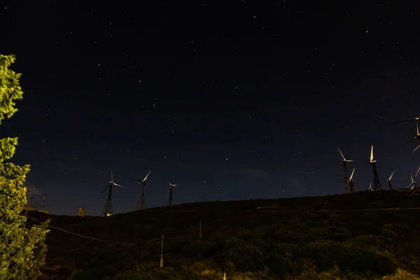 白い風力発電機のグループは、風による代替エネルギーを生成する星の背景を持つ黒の夜空にあります — ストック写真